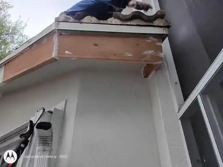 Licensed roofing contractor removing storm-damaged tile pieces from Santa Ana home eave after October wind event, ladder and tools visible