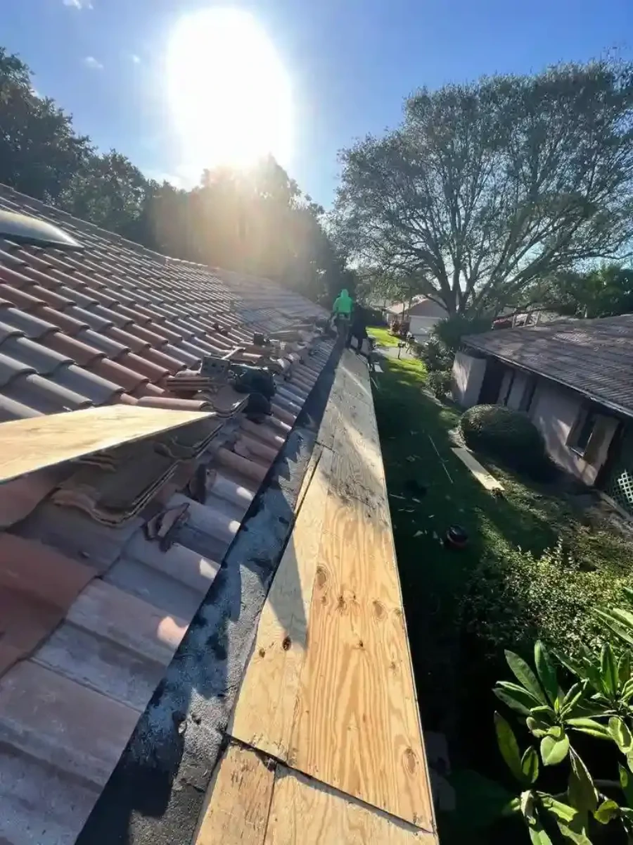 Two-man crew carefully removing and stacking original clay tiles on Santa Ana home during underlayment relay, pool and garden visible below in late afternoon light